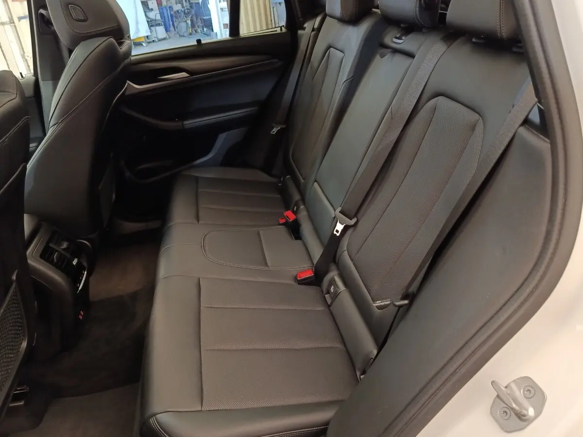 Vue intérieure côté droit des sièges arrière en cuir noir du BMW X3 blanc xDrive30e 2023, avec ceinture de sécurité visible.