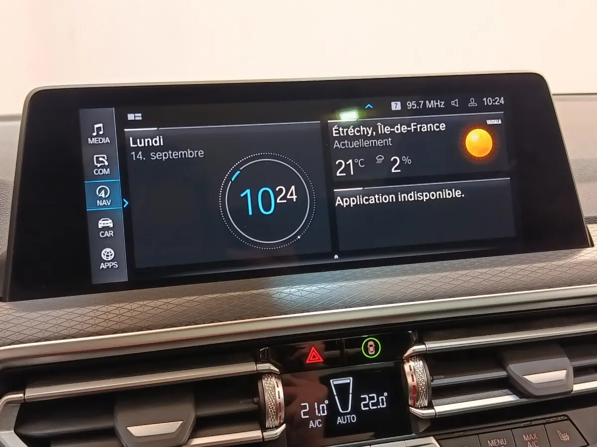 Vue rapprochée du tableau de bord numérique du BMW X3 blanc, affichant l’heure et la météo sur écran tactile.