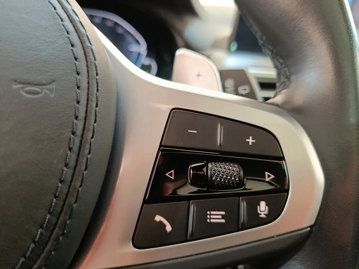 Gros plan sur les commandes du volant en cuir noir du BMW X3 blanc, avec boutons de volume et téléphone.