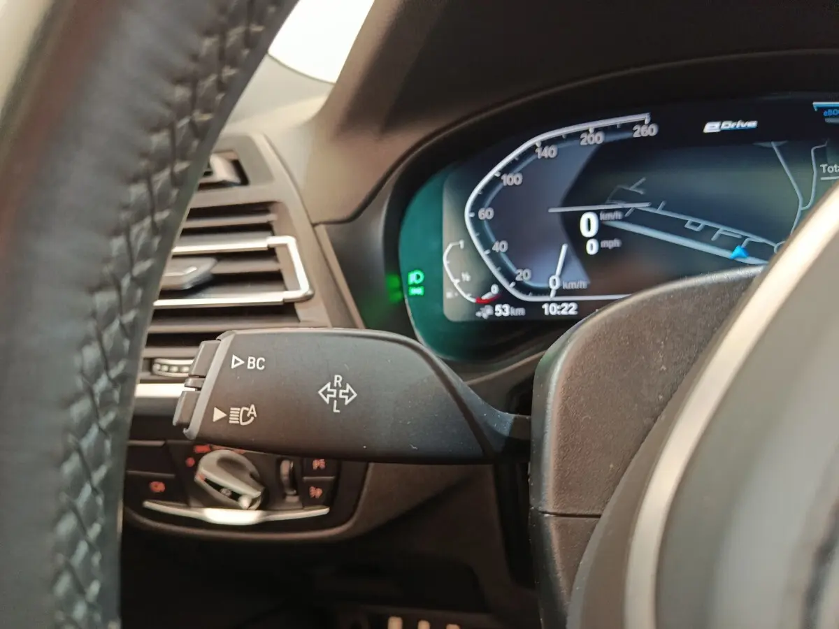 Gros plan sur le combiné d'instruments digital et la commande de clignotants du BMW X3 blanc xDrive30e 2023.