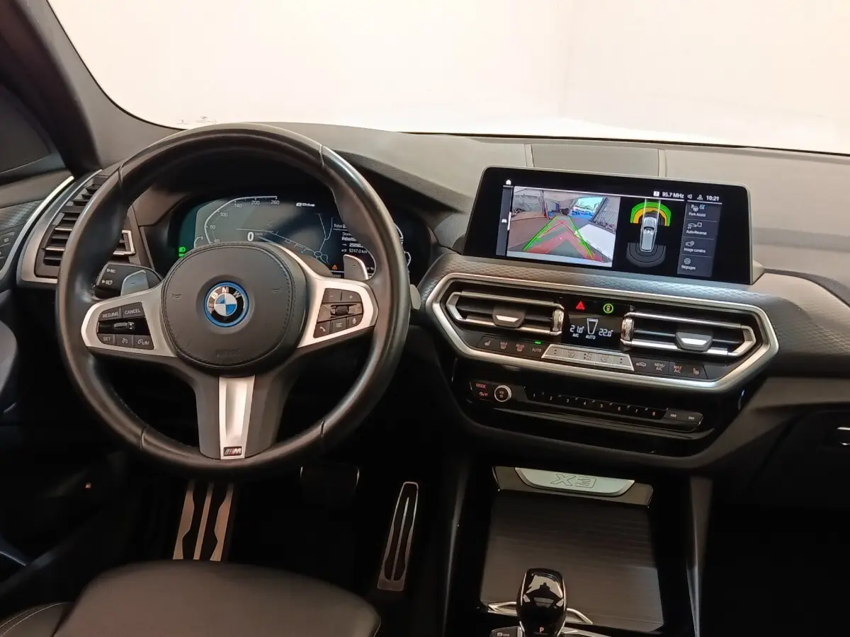 Vue intérieure du tableau de bord et volant cuir noir du BMW X3 xDrive30e avec écran tactile central allumé.