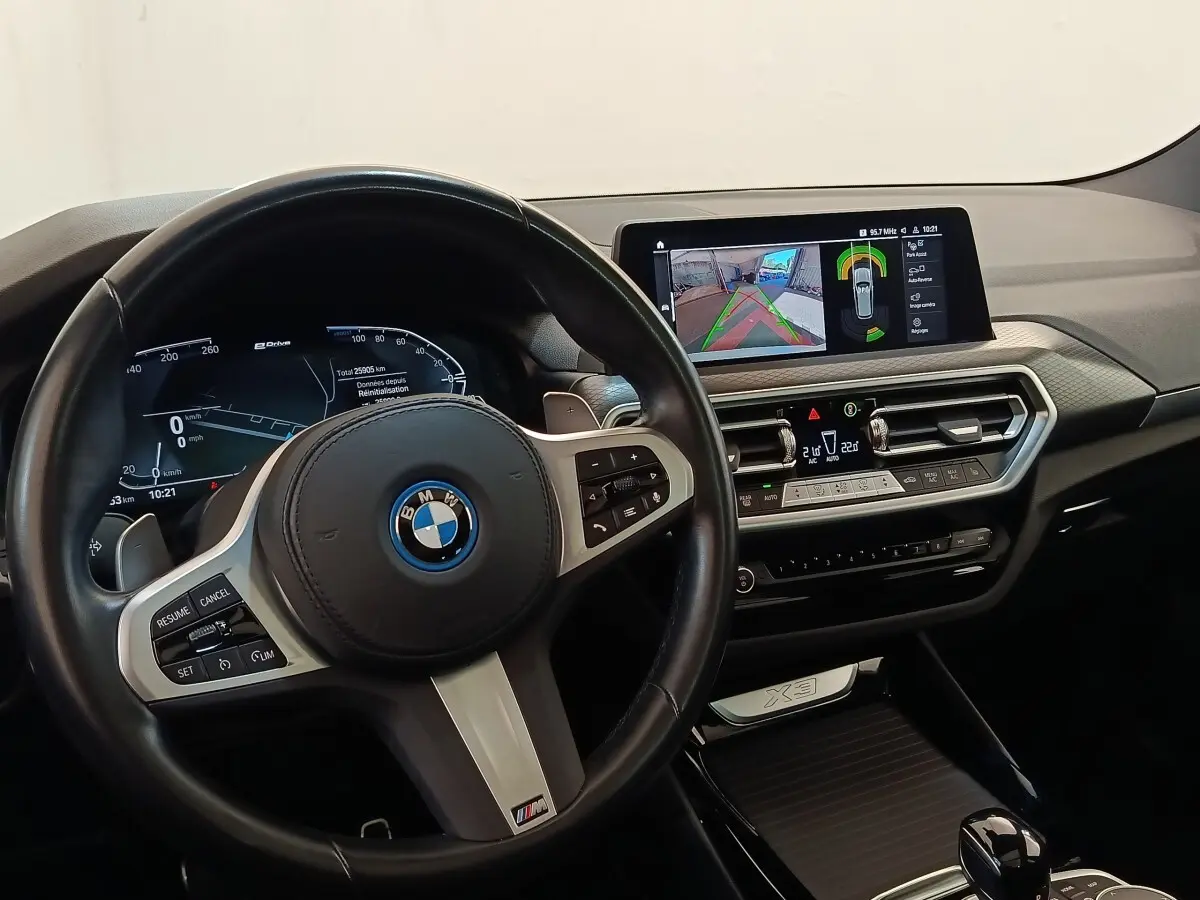 Vue intérieure du tableau de bord et volant cuir noir de la BMW X3 xDrive30e 2023 avec écran tactile et affichage numérique.