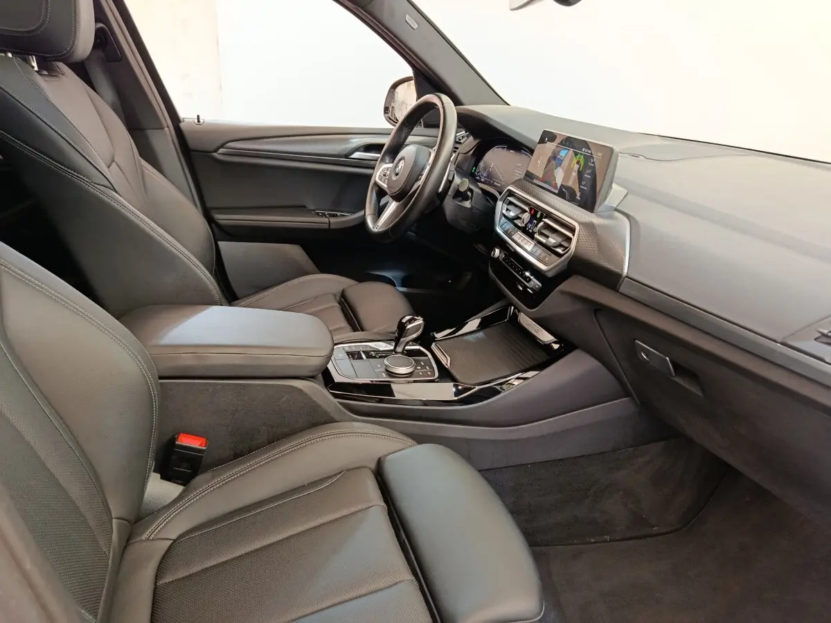 Intérieur BMW X3 xDrive30e 2023 vu côté passager, sièges cuir noirs et tableau de bord avec écran tactile.