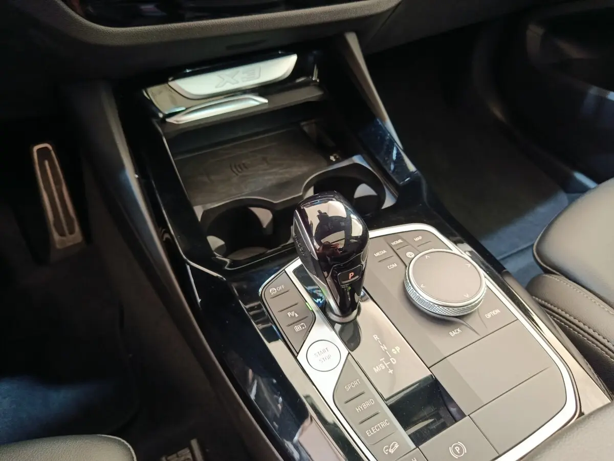 Gros plan sur la console centrale noire du BMW X3 blanc, avec levier de vitesses et molette de contrôle visibles.