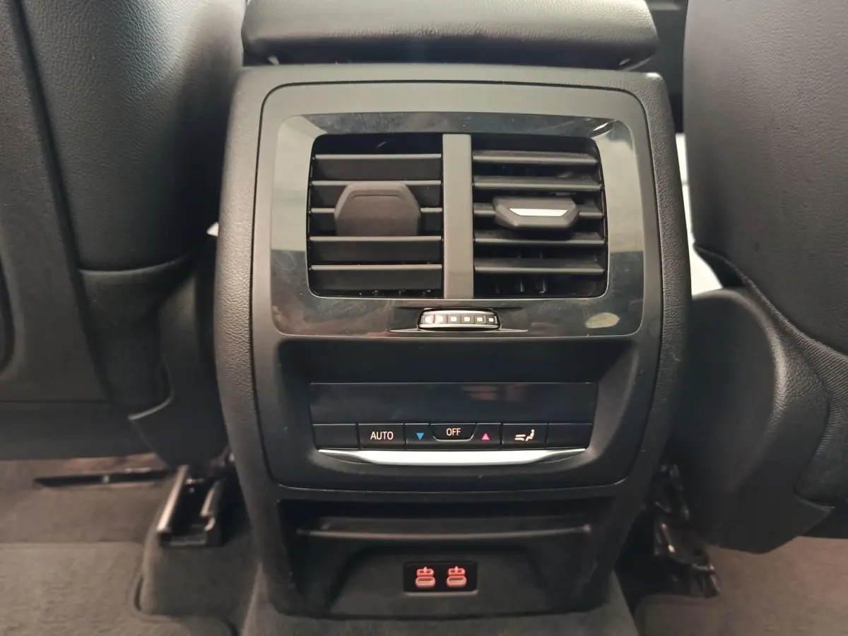 Vue rapprochée de la console arrière noire avec bouches d’aération et commandes climatisation du BMW X3 blanc 2023.