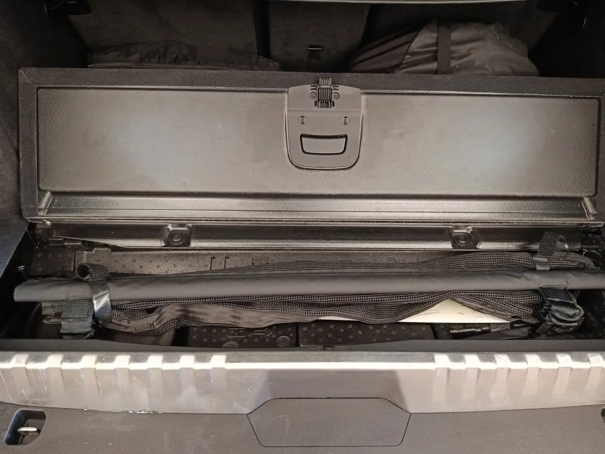 Coffre ouvert d’un BMW X3 blanc, montrant un compartiment de rangement sous plancher avec filet de sécurité noir.