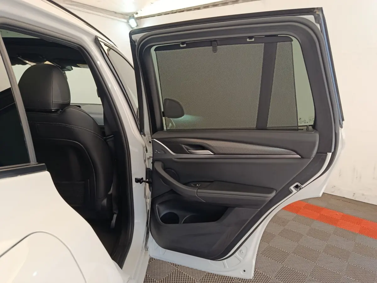 Porte arrière droite ouverte d’un BMW X3 blanc 2023, montrant l’habillage intérieur noir avec pare-soleil intégré.