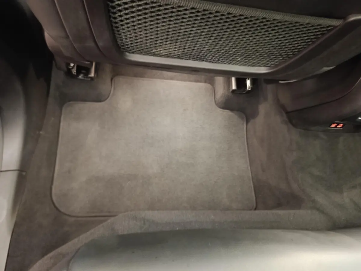 Vue plongeante sur le tapis de sol arrière gris foncé du BMW X3 xDrive30e blanc, avec filet de rangement sous le siège avant.