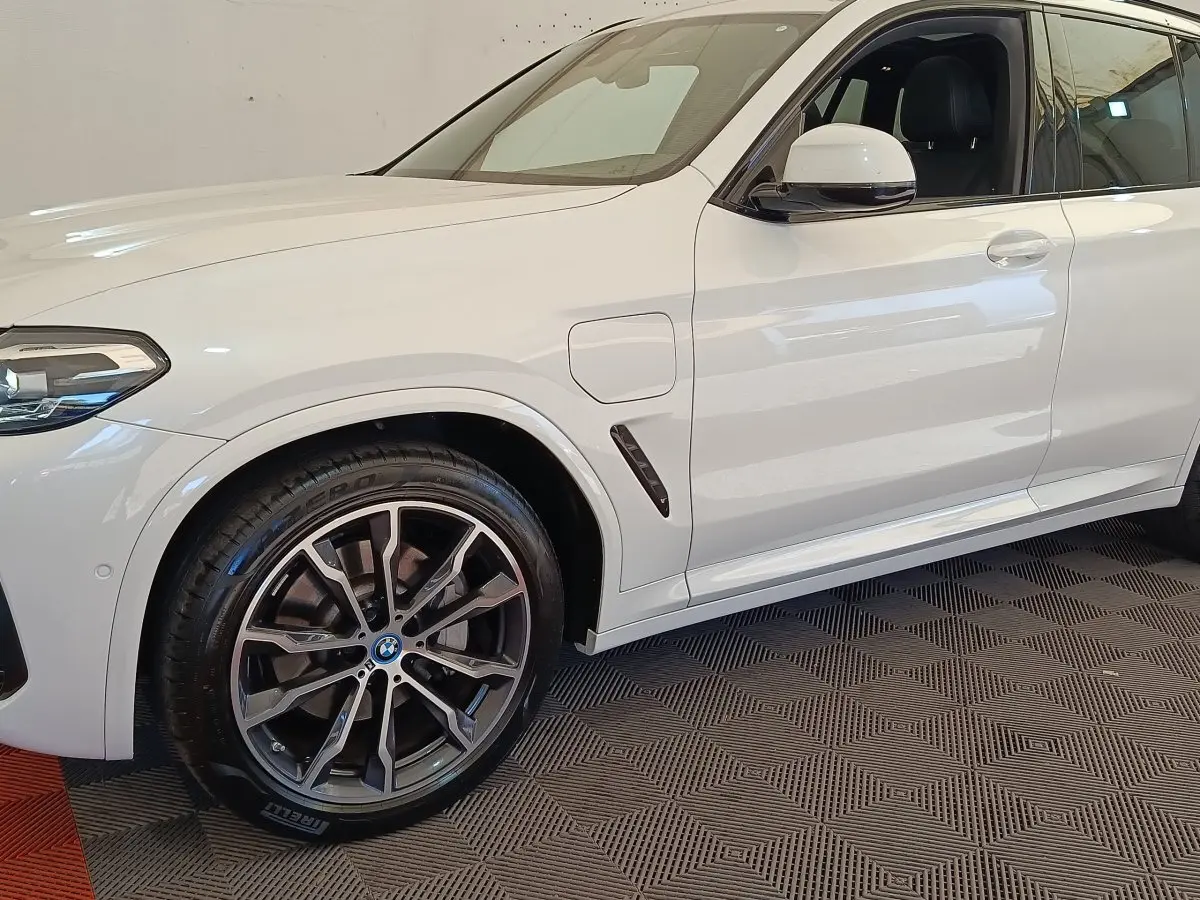 Vue latérale gauche rapprochée du BMW X3 blanc xDrive30e 2023 avec jante alliage et prise de recharge visible.