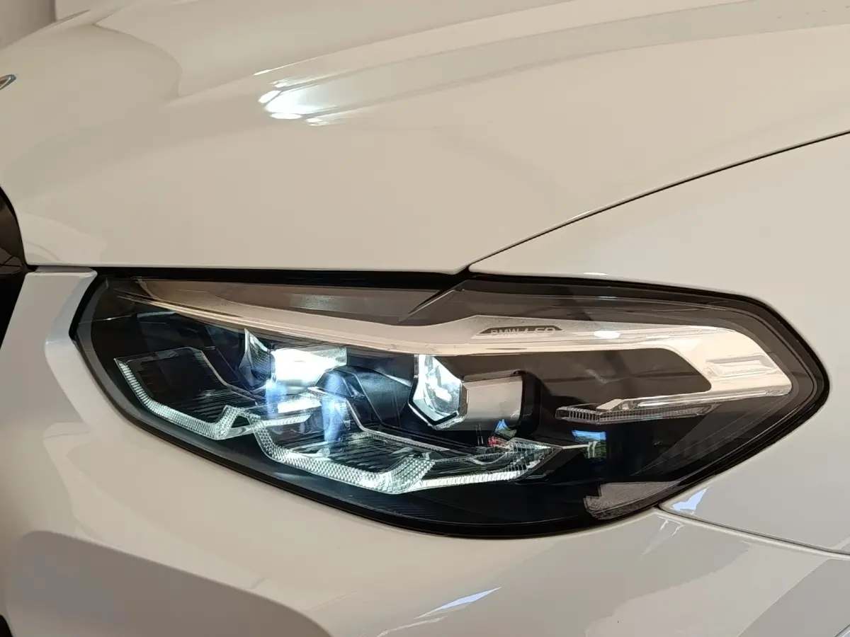 Gros plan sur le phare avant droit LED d’un BMW X3 xDrive30e blanc, mettant en valeur ses détails lumineux modernes.