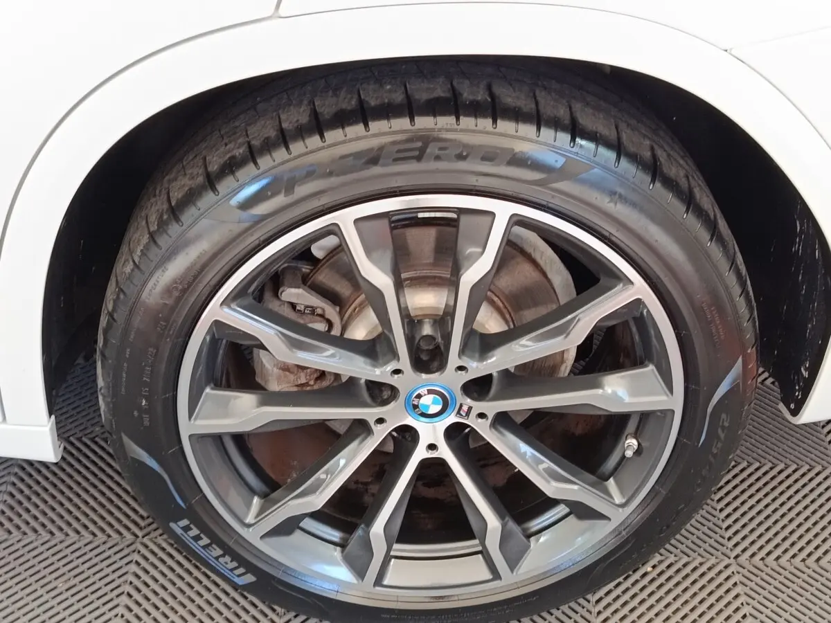 Gros plan sur la roue avant droite d’un BMW X3 blanc avec jante alliage gris foncé et logo M Sport.
