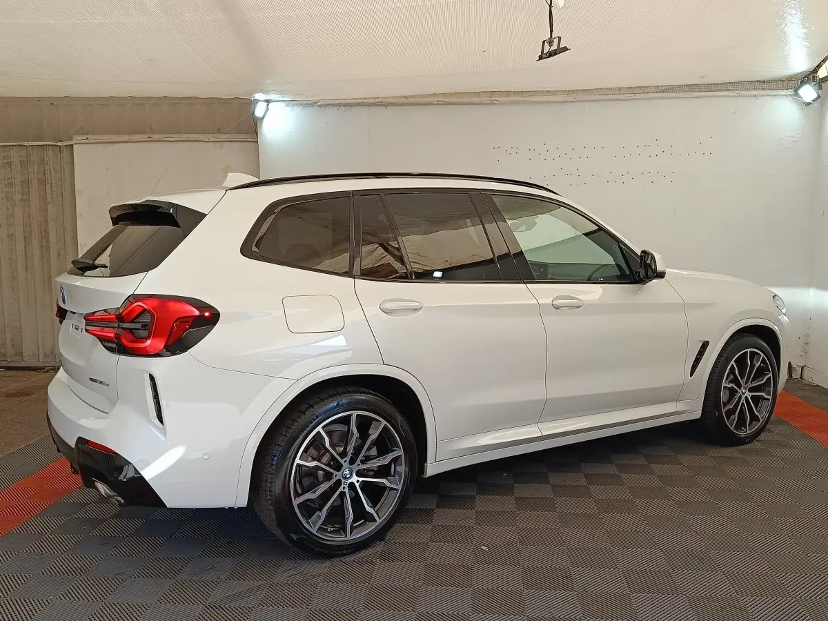 BMW X3 xDrive30e blanc en vue 3/4 arrière droit, avec jantes alliage et feux arrière LED distinctifs.