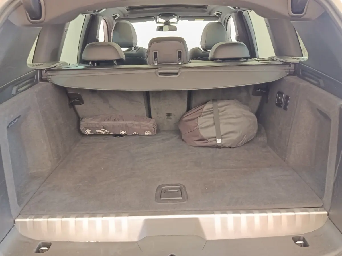 Vue arrière du coffre spacieux d’un BMW X3 blanc 2023 avec cache-bagages et objets rangés.