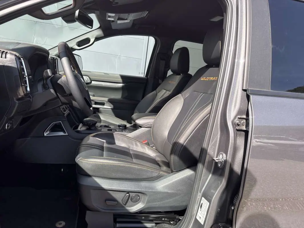 Vue intérieure côté conducteur du Ford Ranger gris carbone 2026, sièges cuir Wildtrak avec surpiqûres orange.