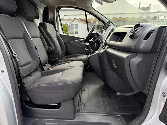 Vue intérieure côté conducteur du Renault Trafic Fourgon gris platine, montrant les sièges avant et le tableau de bord.