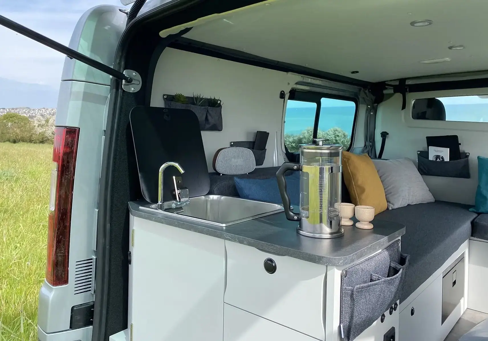 Intérieur du Renault Trafic gris platine, vue arrière ouverte montrant cuisine compacte avec évier et espace détente aménagé.