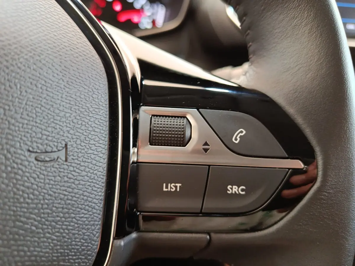 Gros plan sur les commandes multifonctions noires du volant cuir d’une Peugeot 208 blanche, version PureTech 75 S&S Style 2023.