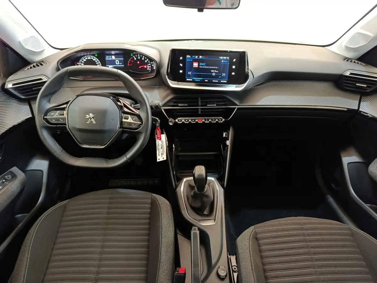 Vue intérieure avant de la Peugeot 208 PureTech 75 Style 2023, tableau de bord noir avec écran tactile central et volant cuir.