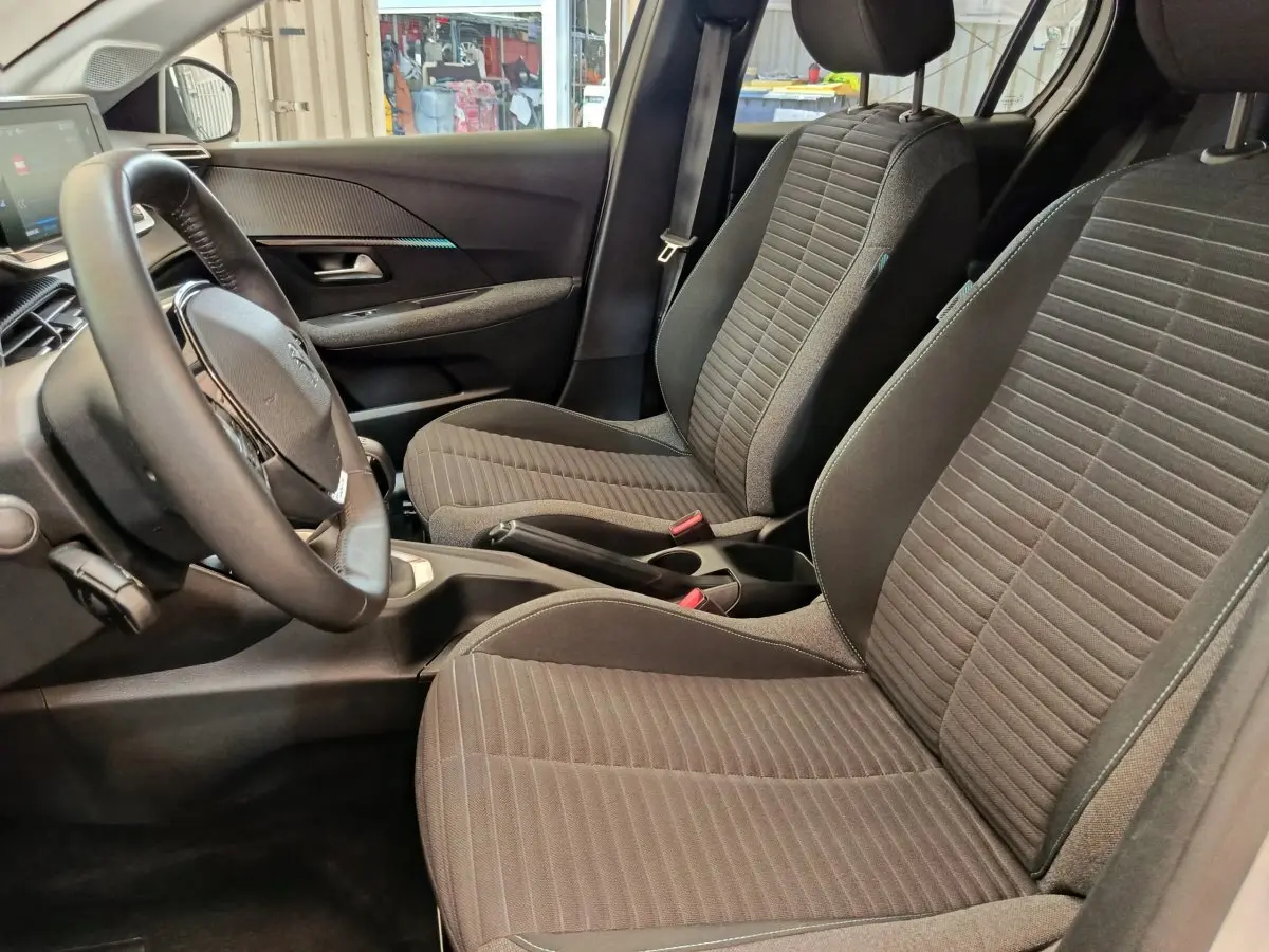 Vue intérieure côté conducteur de la Peugeot 208 PureTech 75 S&S Style 2023, sièges tissu gris et volant cuir.