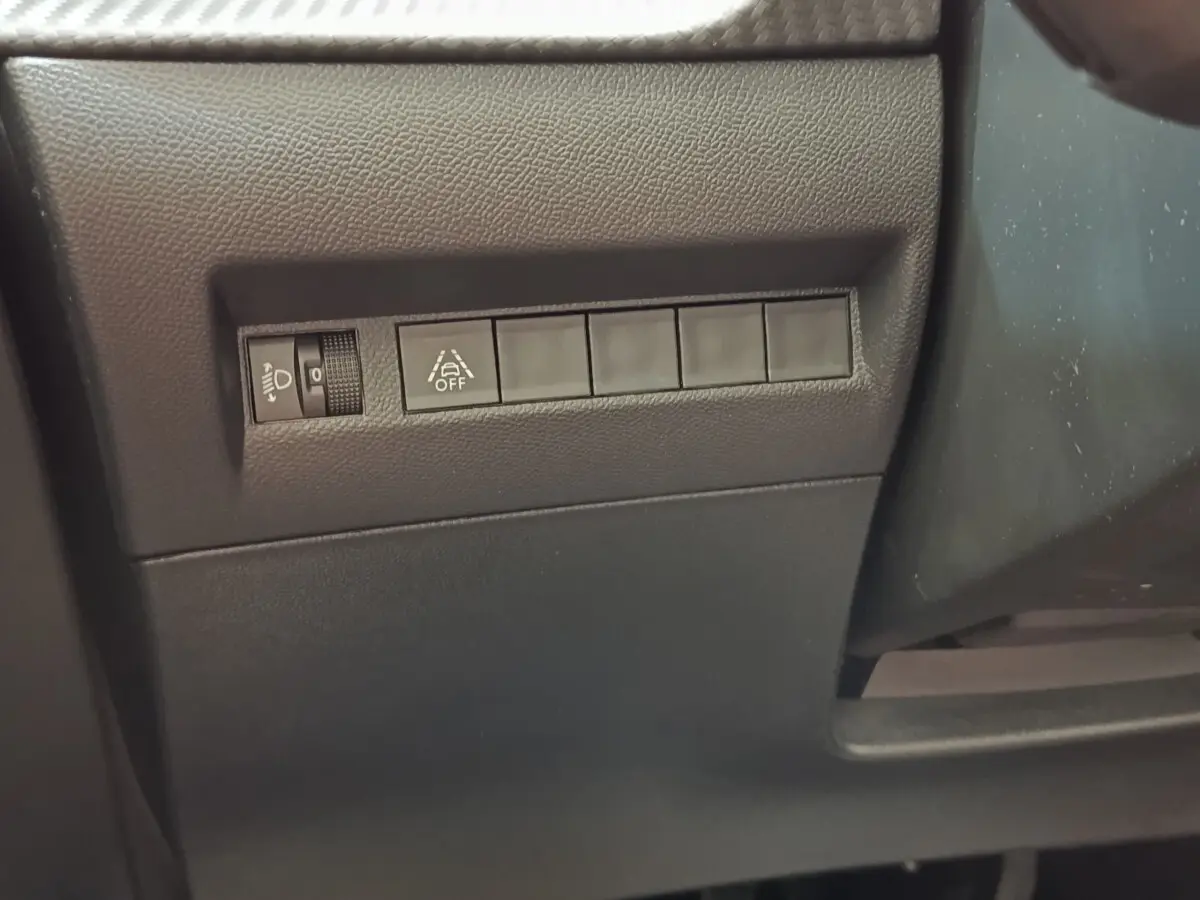 Vue rapprochée des commandes de réglage des phares et de l'alerte de franchissement de ligne sur Peugeot 208 blanc 2023.