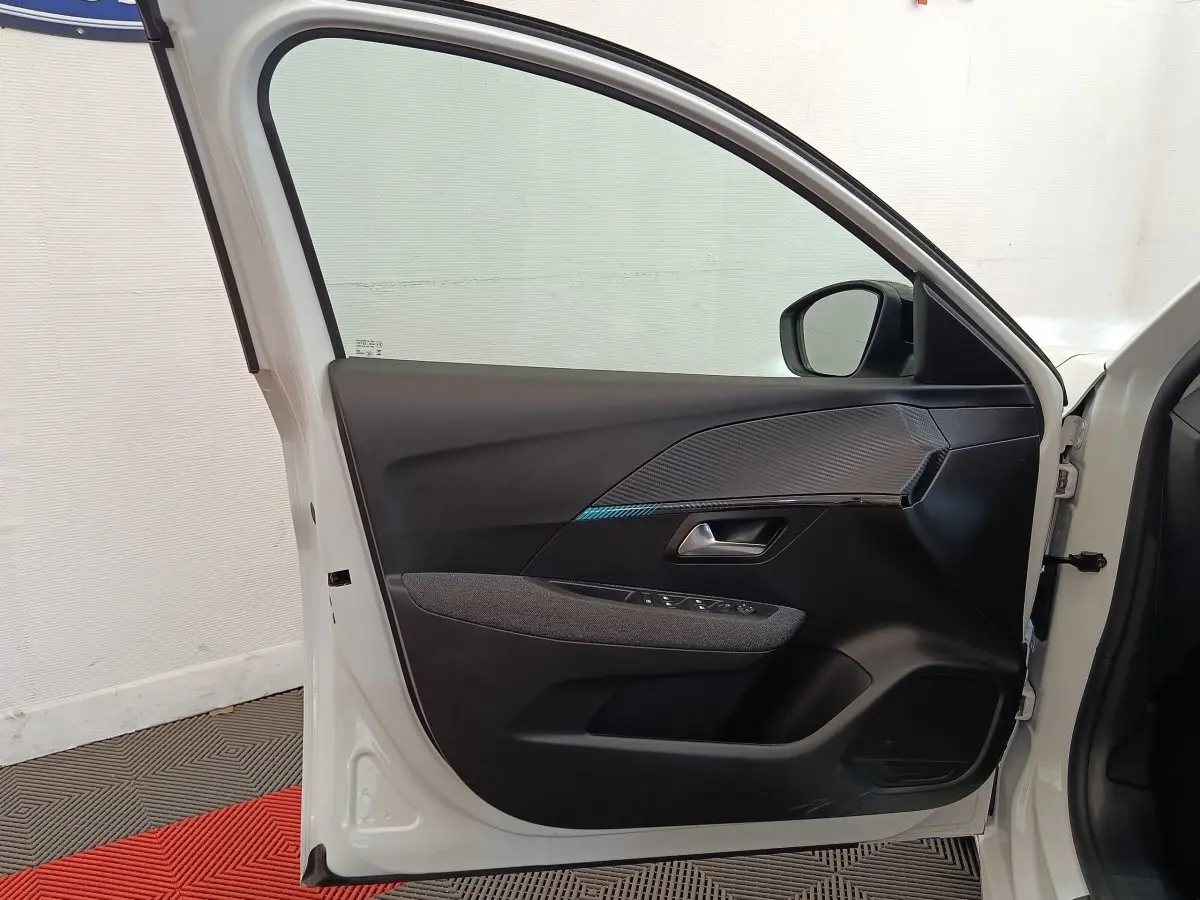 Vue intérieure de la porte avant gauche blanche d'une Peugeot 208 2023 avec garniture noire et détails texturés.