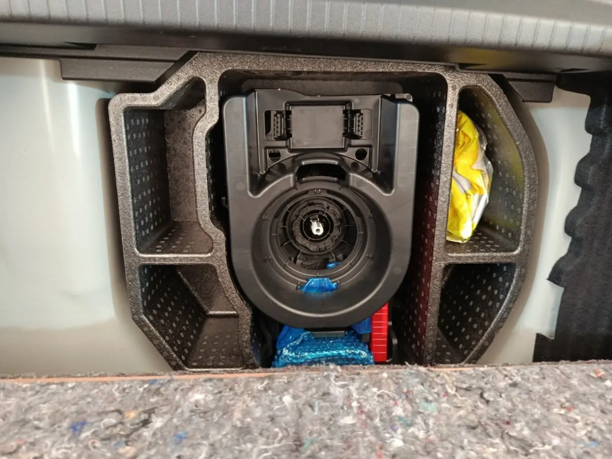 Vue rapprochée du compartiment de rangement sous le plancher de coffre d'une Peugeot 208 blanche, 2023.