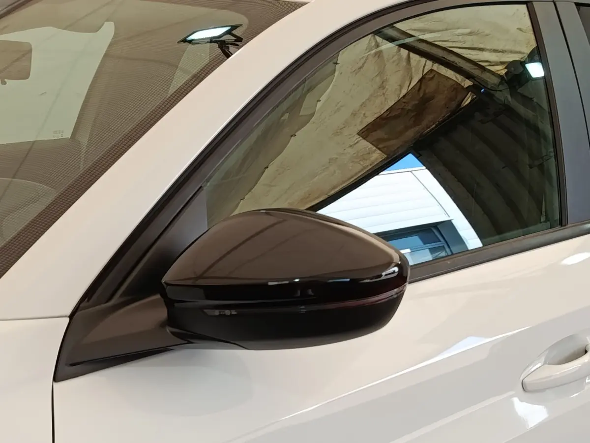 Rétroviseur noir brillant côté conducteur d'une Peugeot 208 blanche PureTech 75 S&S Style 2023, vue latérale rapprochée.