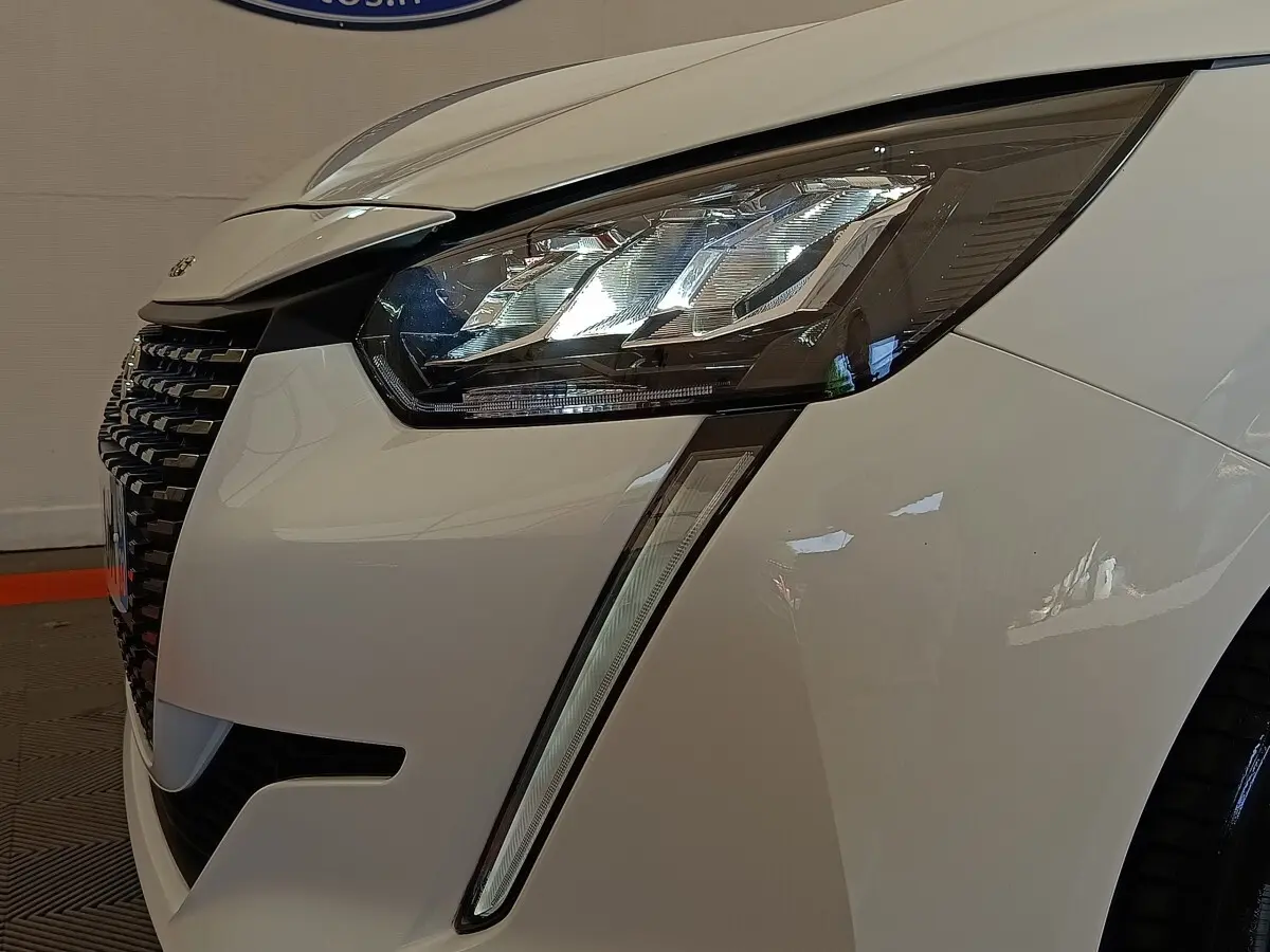 Gros plan sur l'avant droit blanc d'une Peugeot 208 2023, mettant en valeur le phare LED et la calandre noire.