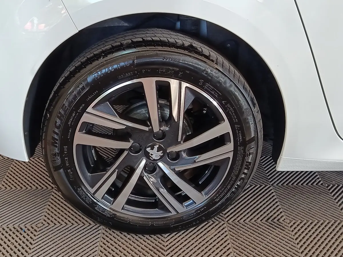 Gros plan sur la roue avant droite d'une Peugeot 208 blanche, avec jante alliage bicolore et pneu Michelin.