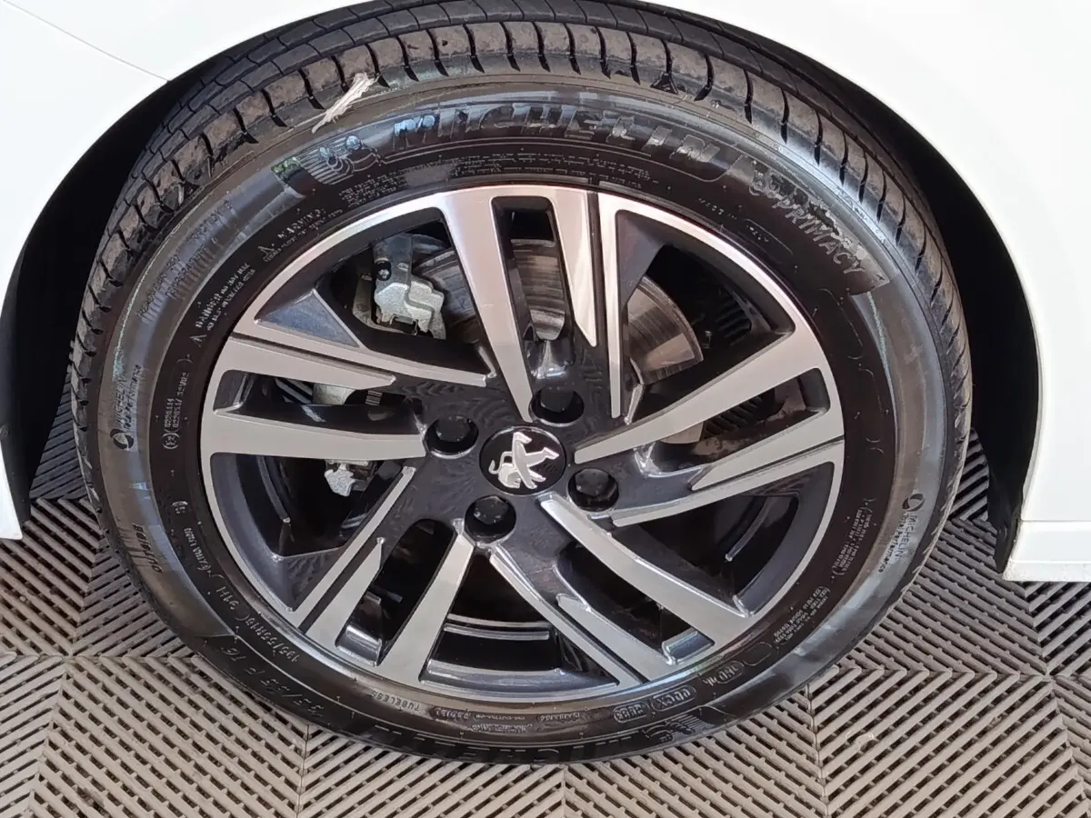 Gros plan sur la roue avant droite de la Peugeot 208 blanche, mettant en valeur la jante alliage noire et argentée au logo lion.