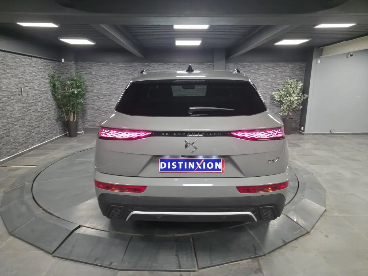 Vue arrière du DS7 Crossback gris avec feux arrière LED 3D et logo DS Automobiles sur fond intérieur showroom.
