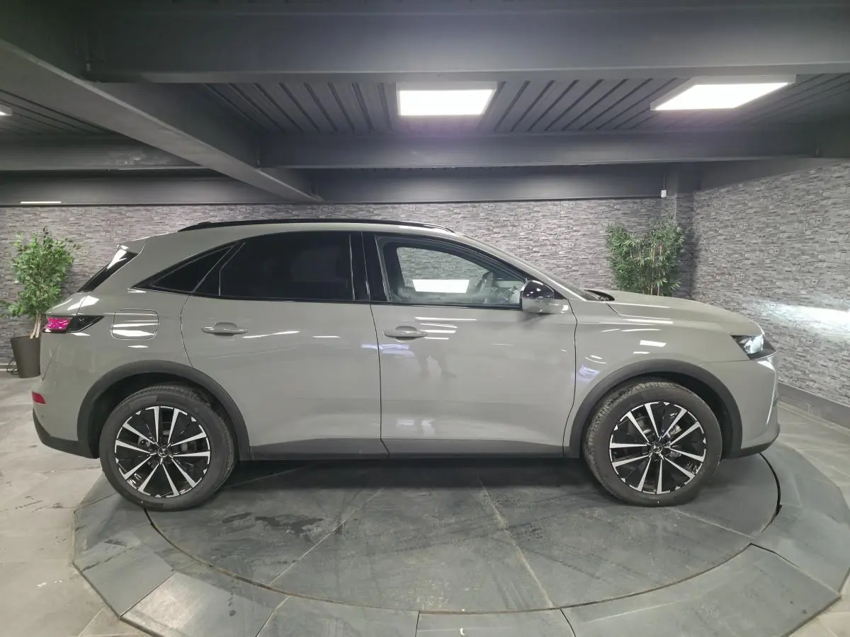Vue de profil côté gauche du DS7 Crossback gris métallisé avec jantes alliage noires et toit noir en intérieur showroom.