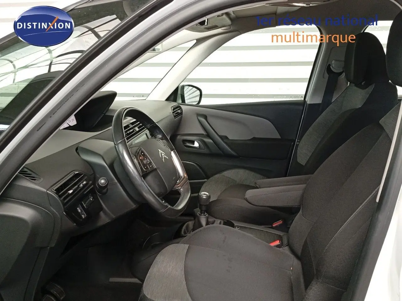 Intérieur avant du Citroën Grand C4 Picasso blanc 2016, vue côté conducteur avec volant et sièges tissu noir et gris.