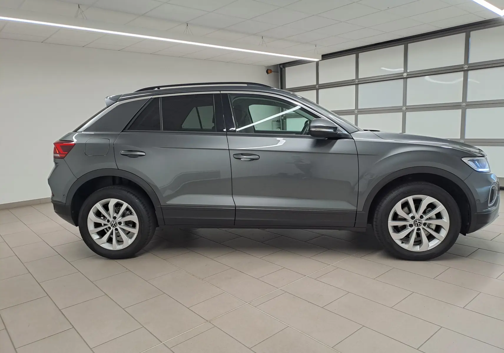 Profil droit du Volkswagen T-Roc 2024 en gris Indium métallisé avec jantes alliage 17'' Johannesburg dans un garage.