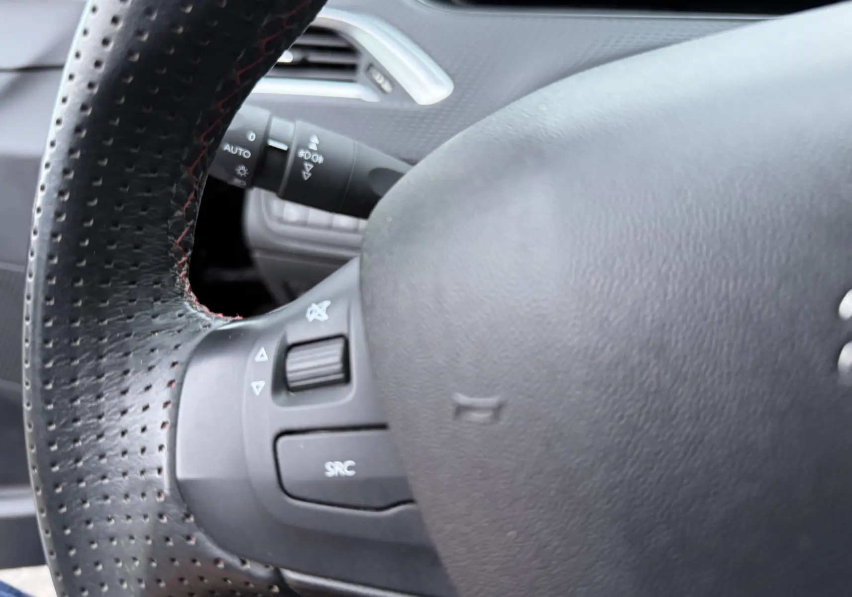 Gros plan sur le volant noir perforé du Peugeot 2008 1.2 PureTech 110 GT Line, avec commandes intégrées visibles.