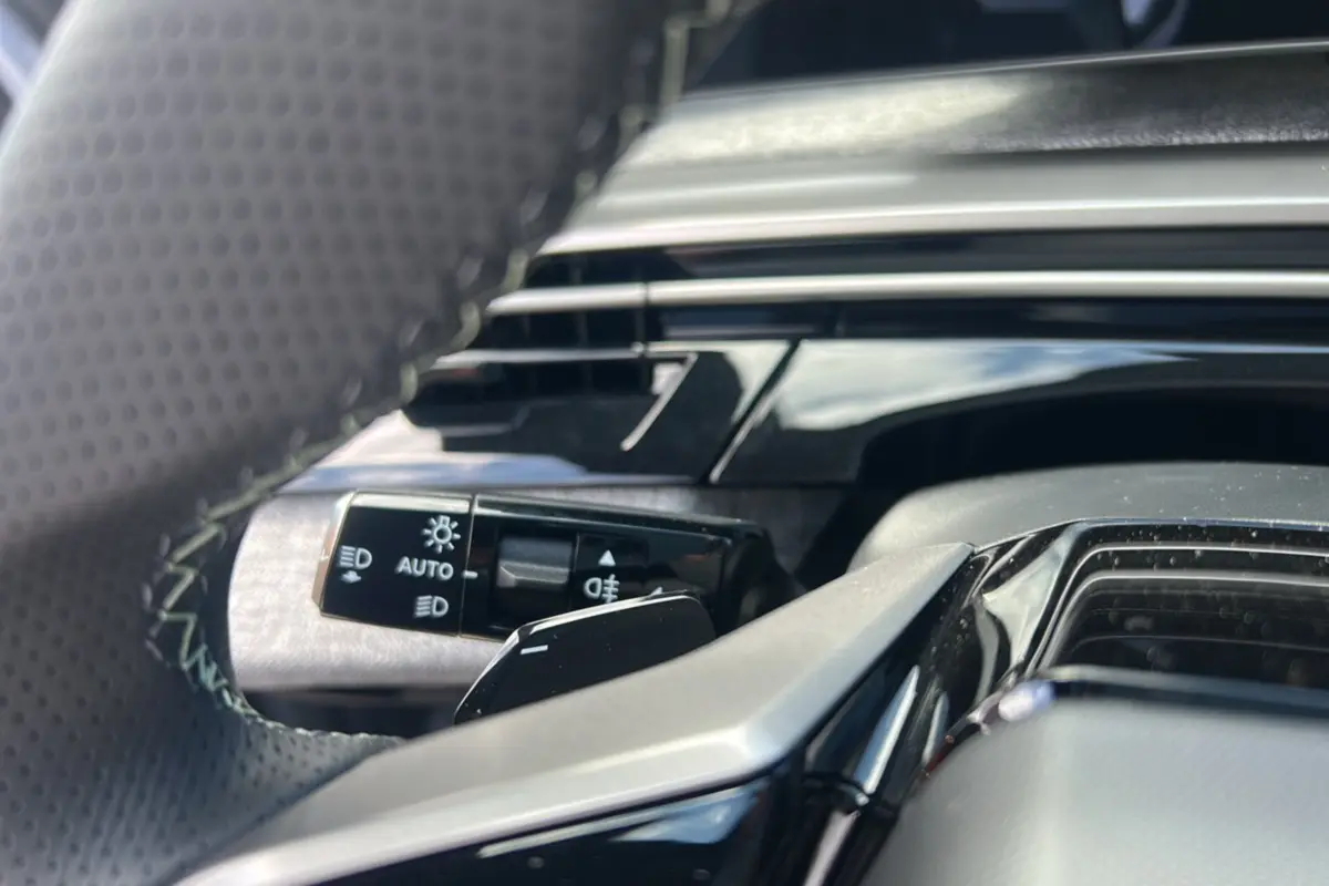 Gros plan sur la commande des feux et clignotants derrière le volant cuir perforé du Peugeot 5008 gris Artense.