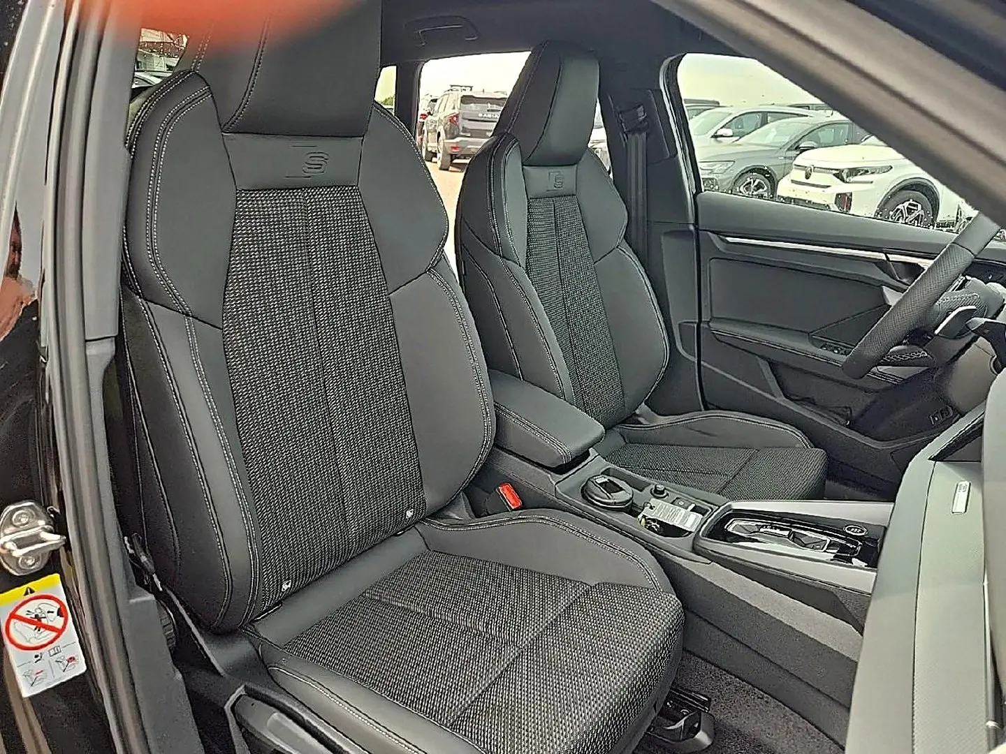 Vue intérieure avant de l'Audi A3 Sportback 2026 noir mythos, sièges sport S avec surpiqûres blanches et console centrale.
