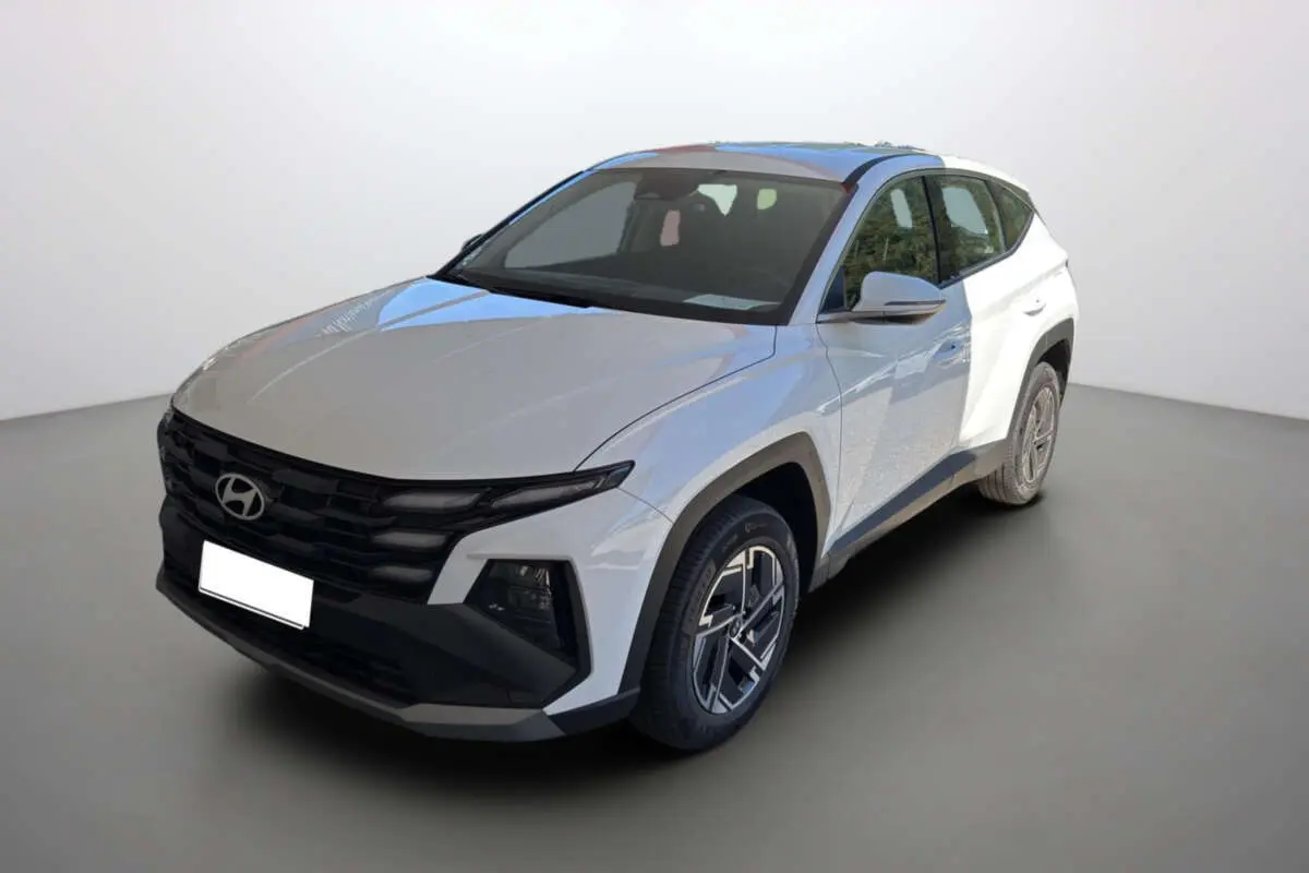 Hyundai Tucson blanc atlas en 3/4 avant droit, avec calandre noire distinctive et jantes alu 17 pouces.