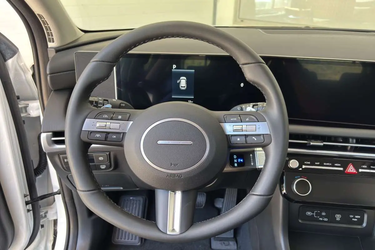 Vue intérieure centrée sur le volant cuir multifonctions du Hyundai Tucson blanc atlas, avec tableau de bord digital.
