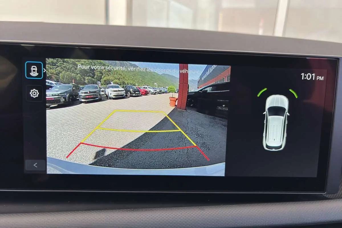 Vue écran caméra de recul du Hyundai Tucson blanc atlas, affichant les lignes d'aide au stationnement et l'alerte de proximité arrière.