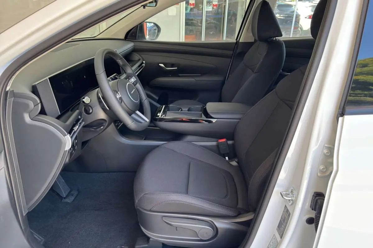 Intérieur côté conducteur du Hyundai Tucson blanc atlas 2026, montrant sièges tissu noirs et tableau de bord moderne.
