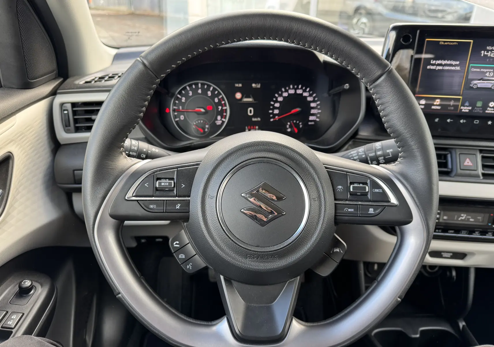 Vue centrée sur le volant noir de la Suzuki Swift 1.2 Hybrid Privilege 2025 avec tableau de bord et écran tactile en arrière-plan.