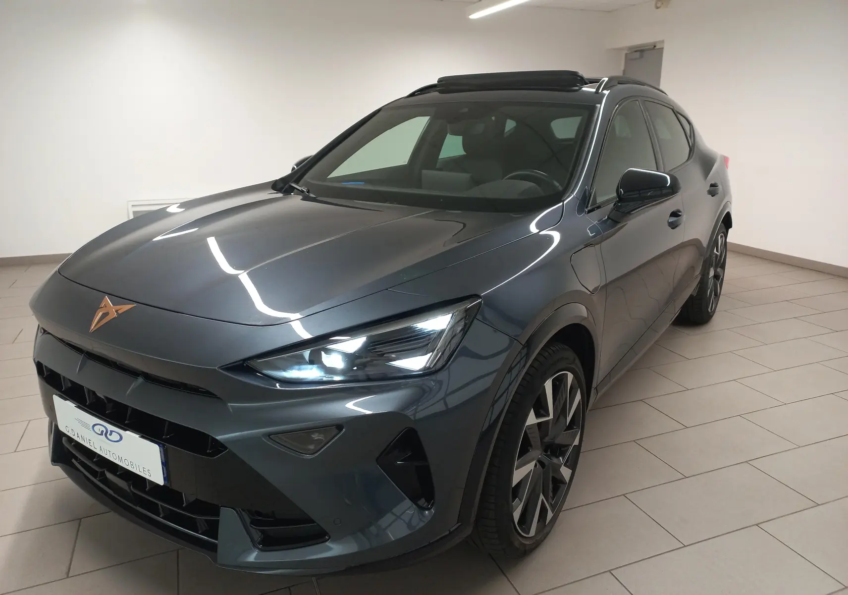 Vue 3/4 avant droite d'un CUPRA Formentor gris magnétique avec toit ouvrant panoramique et phares allumés en intérieur.