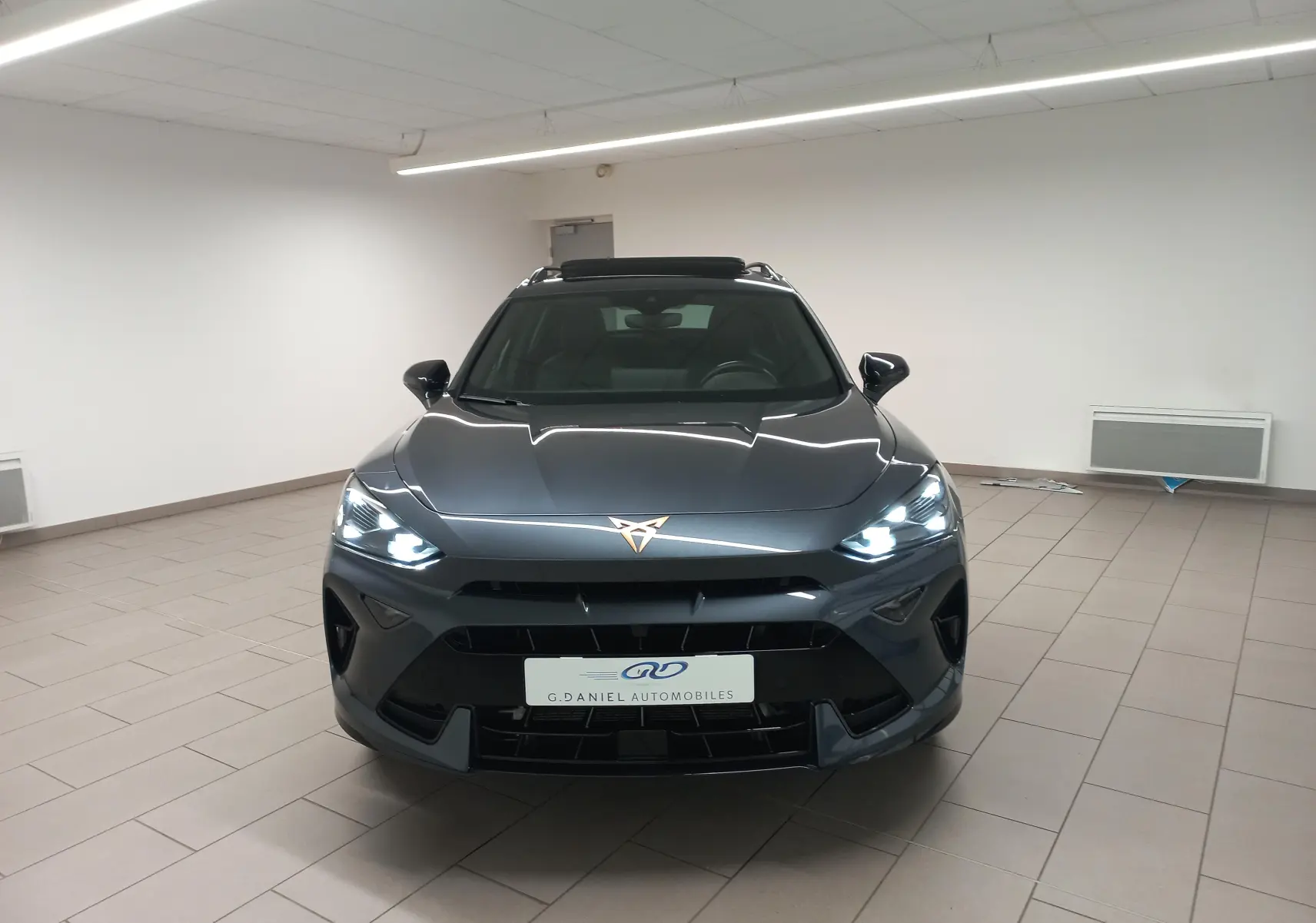 Vue avant d'une CUPRA Formentor gris magnétique avec phares allumés et toit ouvrant panoramique visible en intérieur.