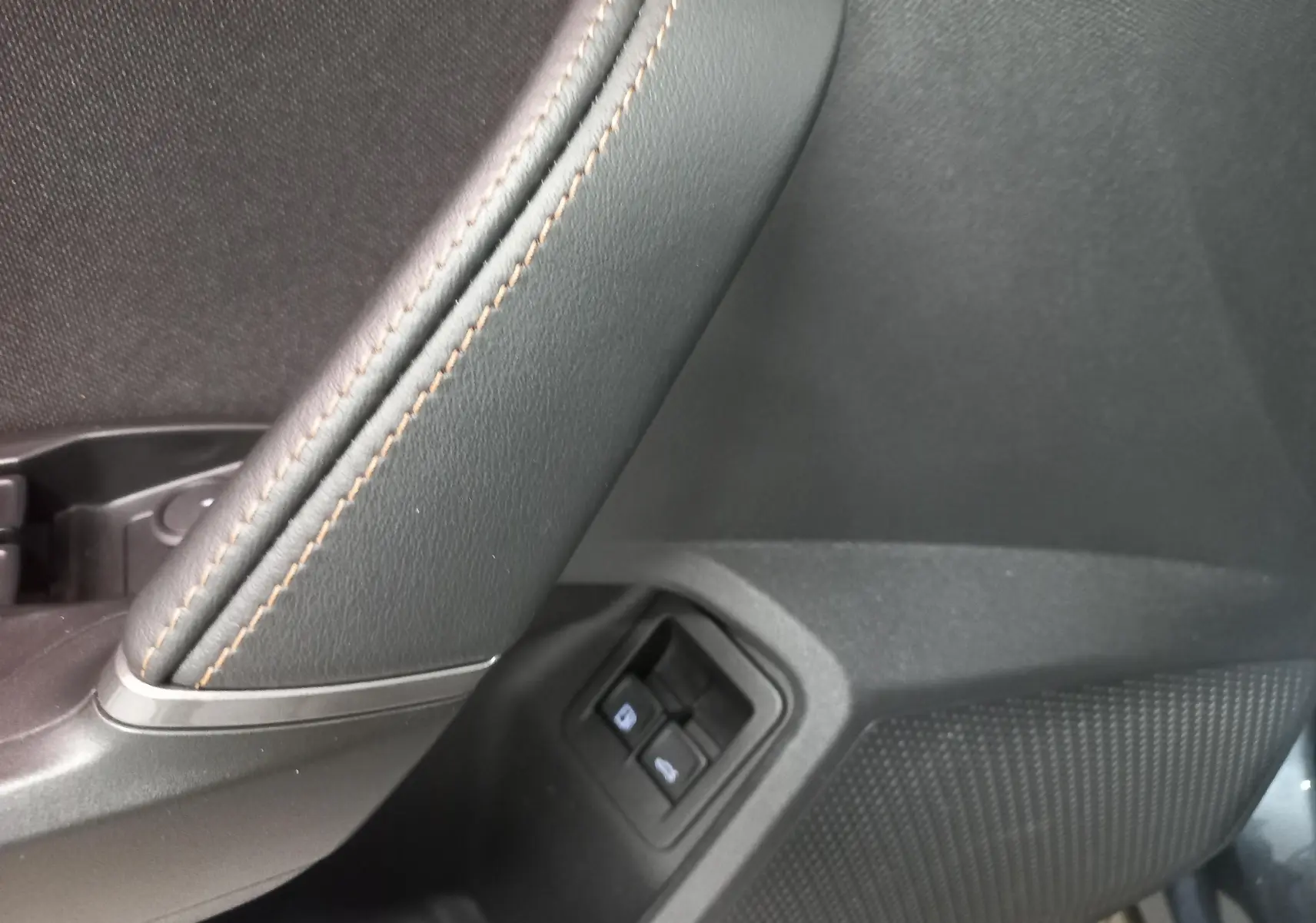 Détail de la commande des vitres côté gauche avec surpiqûres marron sur le revêtement intérieur noir du CUPRA Formentor gris magnétique.