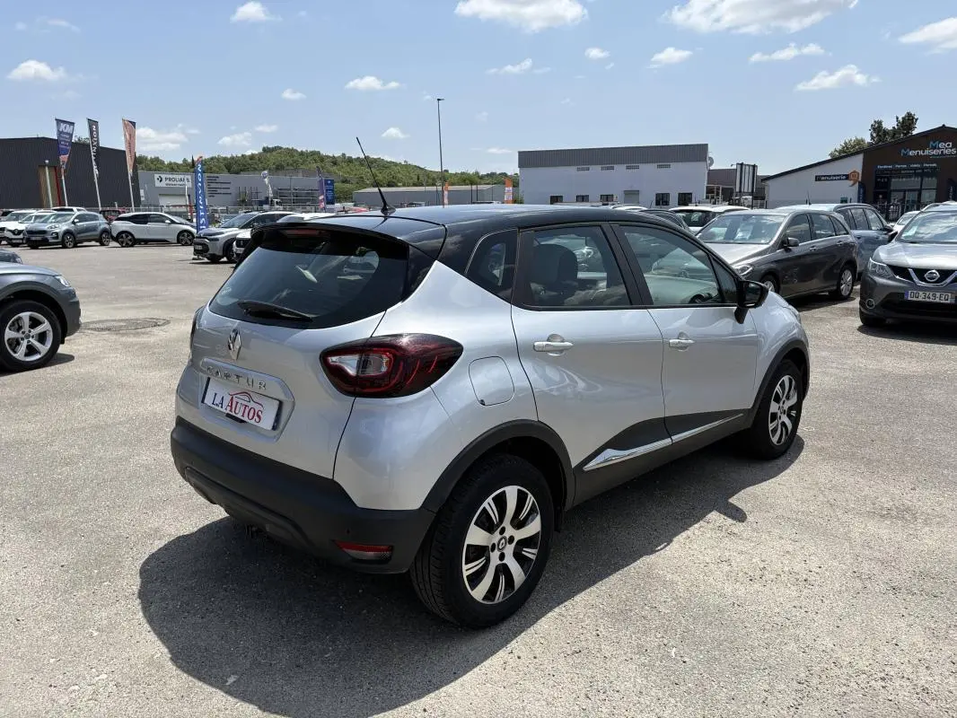 Renault Captur gris vue 3/4 arrière droit, toit noir, jantes aluminium, stationné en extérieur sous ciel clair.