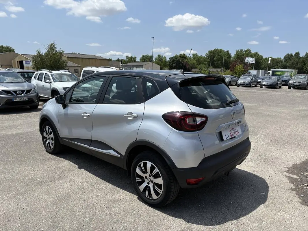 Vue 3/4 arrière droite d'un Renault Captur gris avec toit noir, jantes aluminium et vitres surteintées, stationné en extérieur.