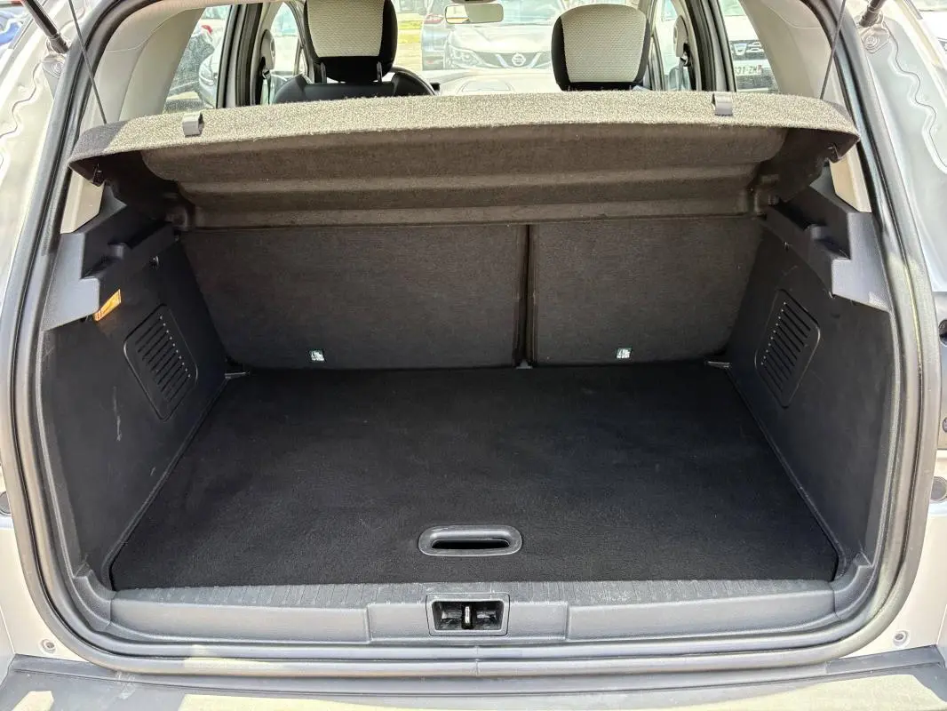 Coffre ouvert vu de l'arrière d'un Renault Captur gris, montrant l'espace de chargement et la tablette cache-bagages relevée.