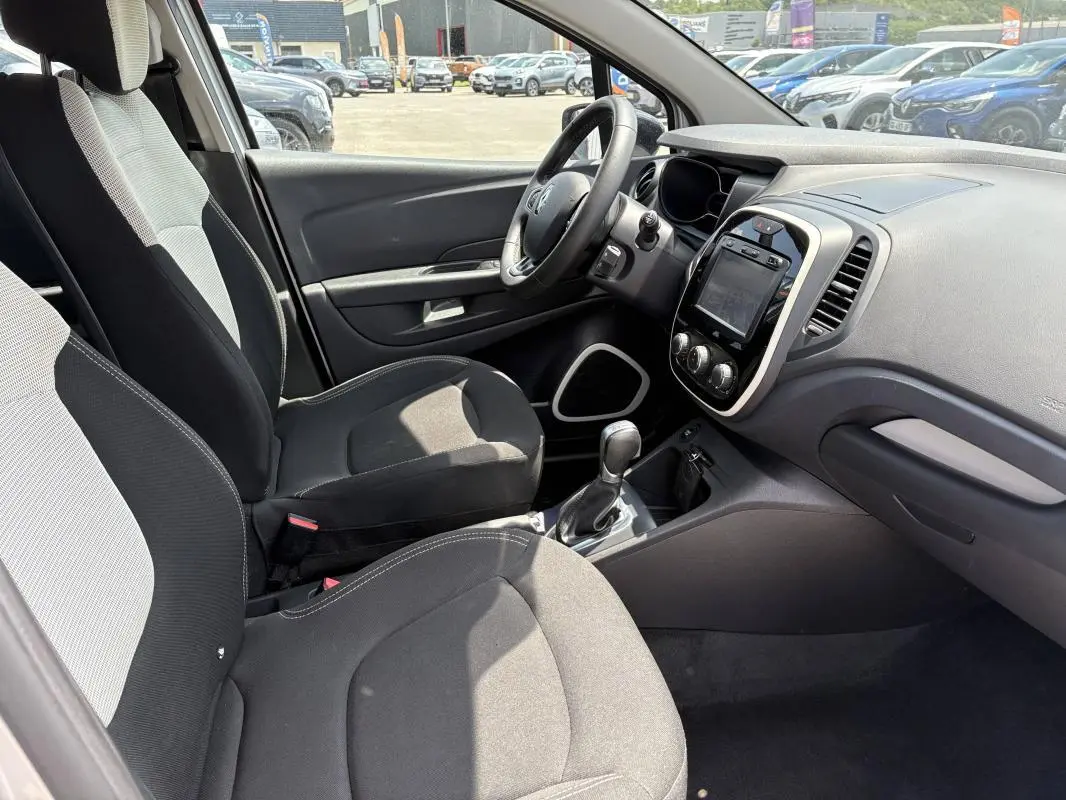Vue intérieure côté conducteur du Renault Captur gris, montrant sièges tissu bicolore et tableau de bord avec écran tactile.