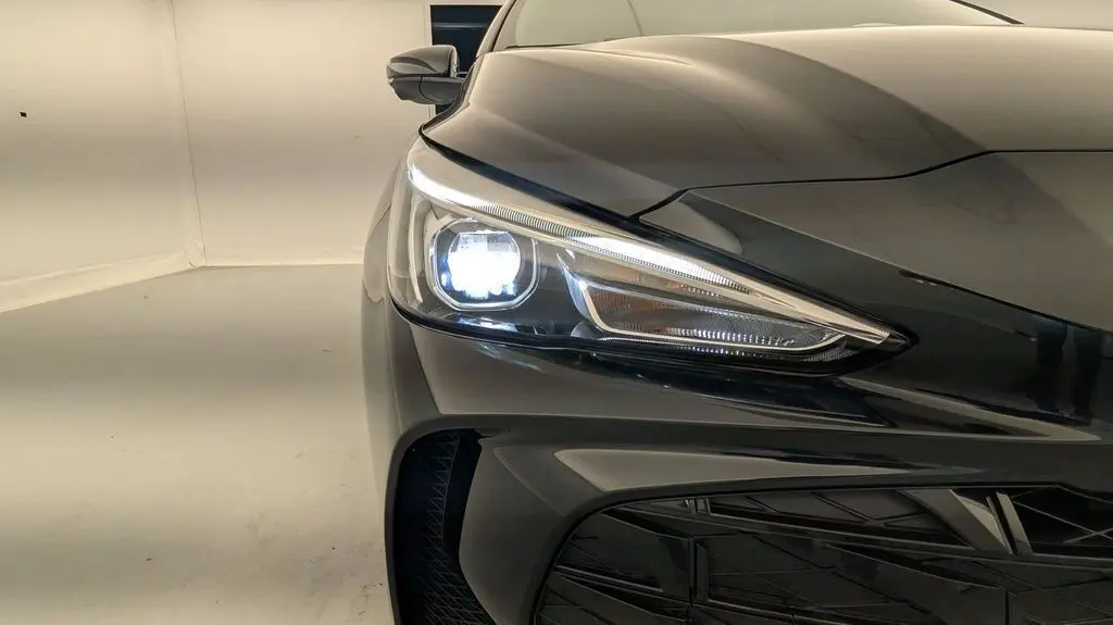 Gros plan sur l'avant gauche du MG3 1.5L Hybrid+ Pebble Black Metal avec phare allumé et calandre noire.